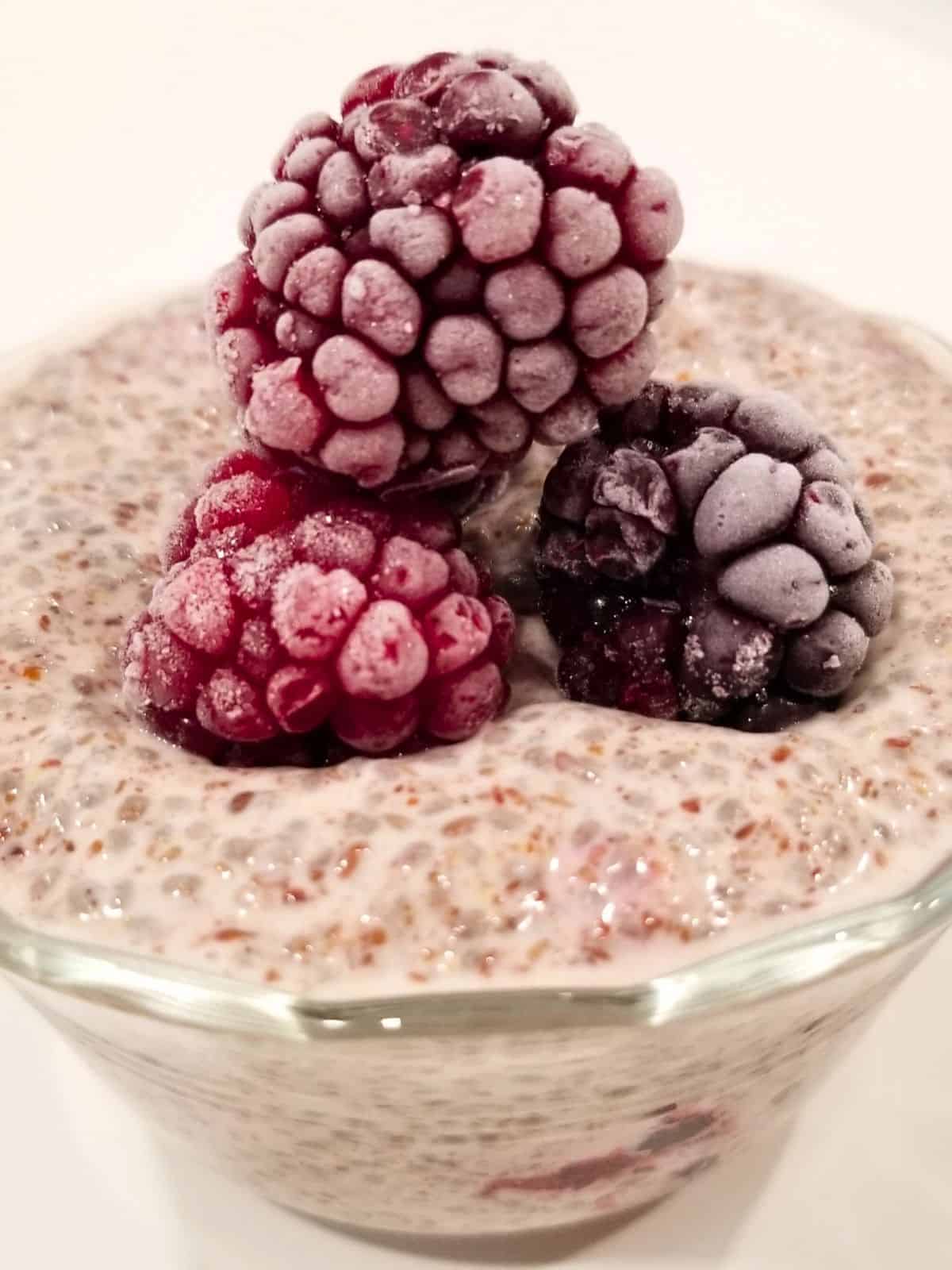 chia and flax seed pudding, topped with frozen berries, in a glass container.