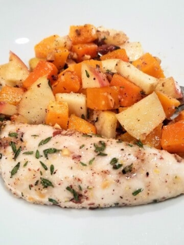 herb-coated chicken, served with baked butternut squash and apples on a plate.