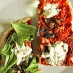 two slices of pizza dough with red pepper sauce, some fresh leaves, and ricotta cheese on a plate.