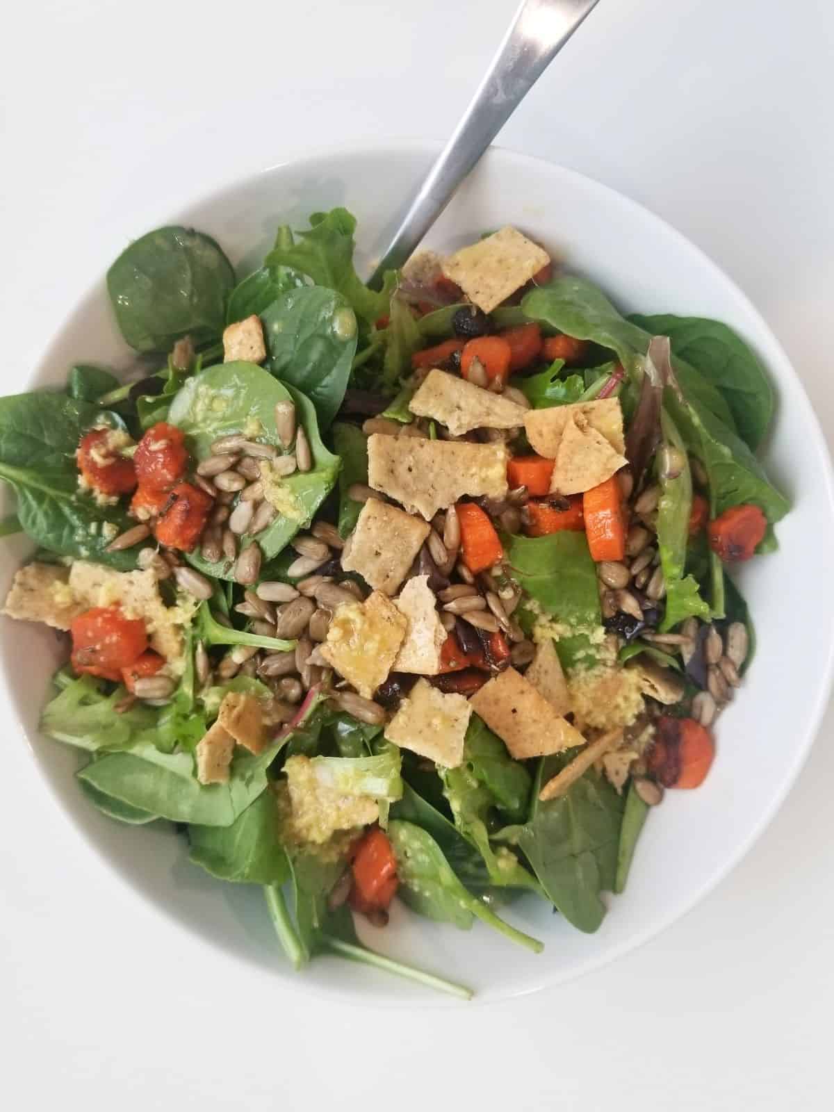 vegetable salad, topped with crackers, seeds, and lemon ginger dressing, in a bowl.