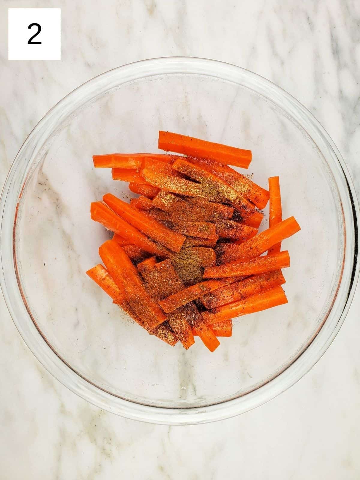 sliced carrots, topped with seasonings, in a large glass bowl.