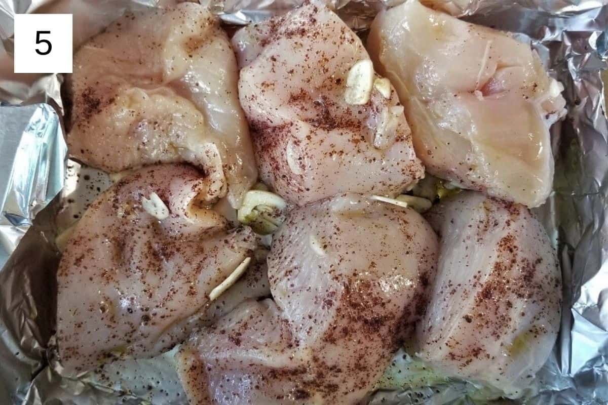 Raw chicken pieces on a baking tray, seasoned with oil, sumac, Italian seasoning, and rosemary.