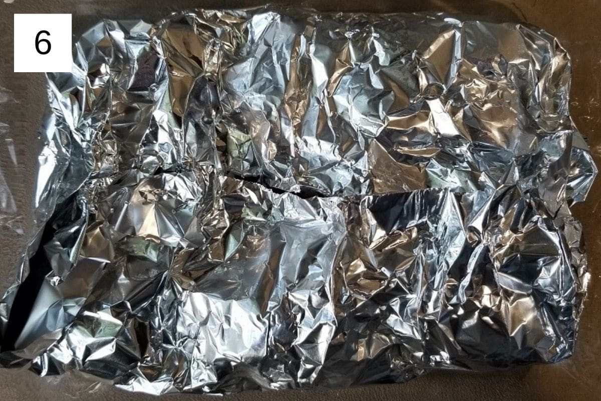 Raw chicken pieces and cauliflower florets on a baking tray, covered with aluminum foil.