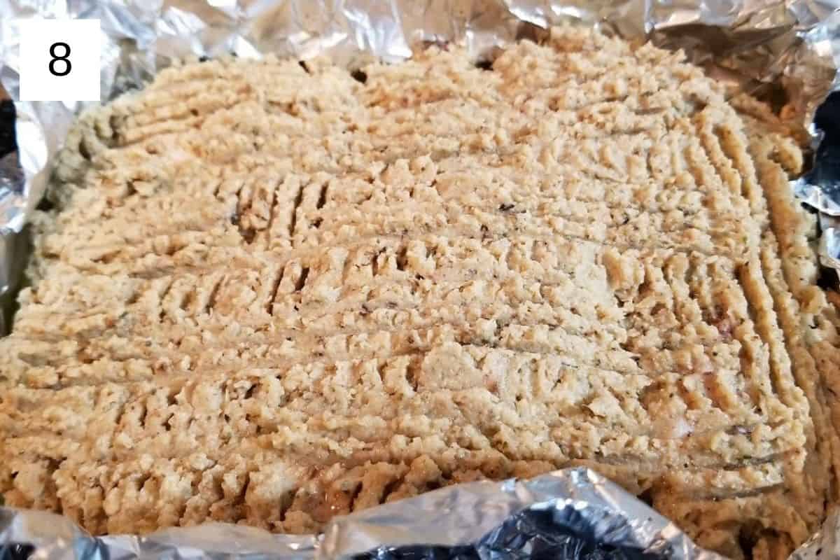 A mixture of baked chicken and cauliflower, flattened on a baking tray.
