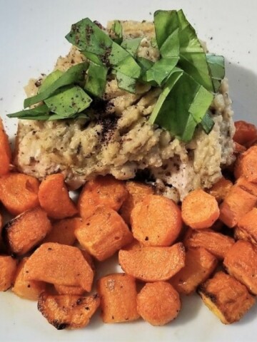Baked chicken and cauliflower on a plate, topped with fresh herbs, and served with blistered carrots.