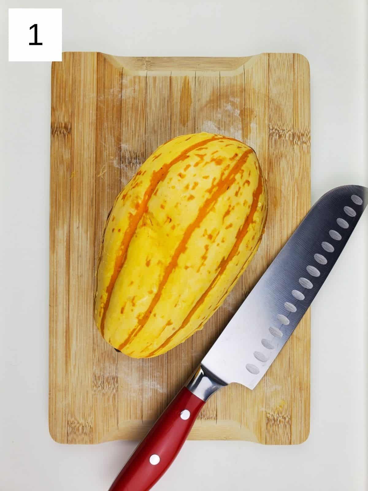 one whole delicata squash on a wooden cutting board.