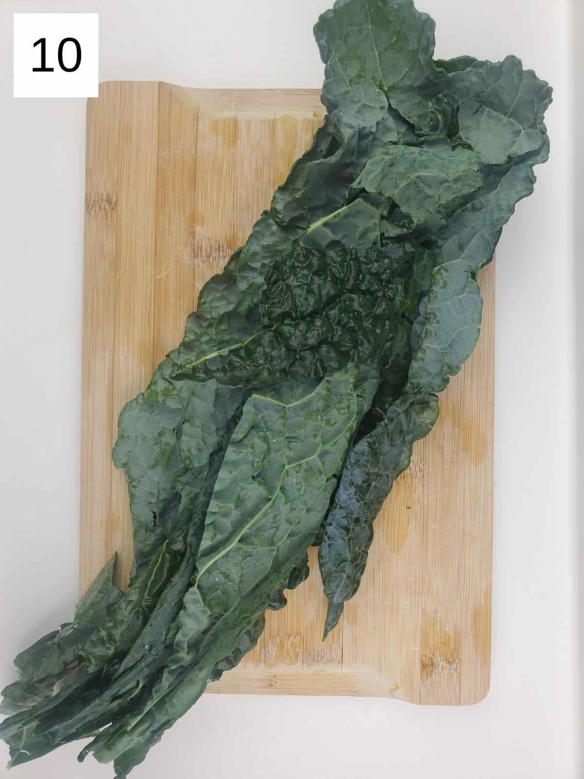 kale leaves with spines removed, on a wooden cutting board.
