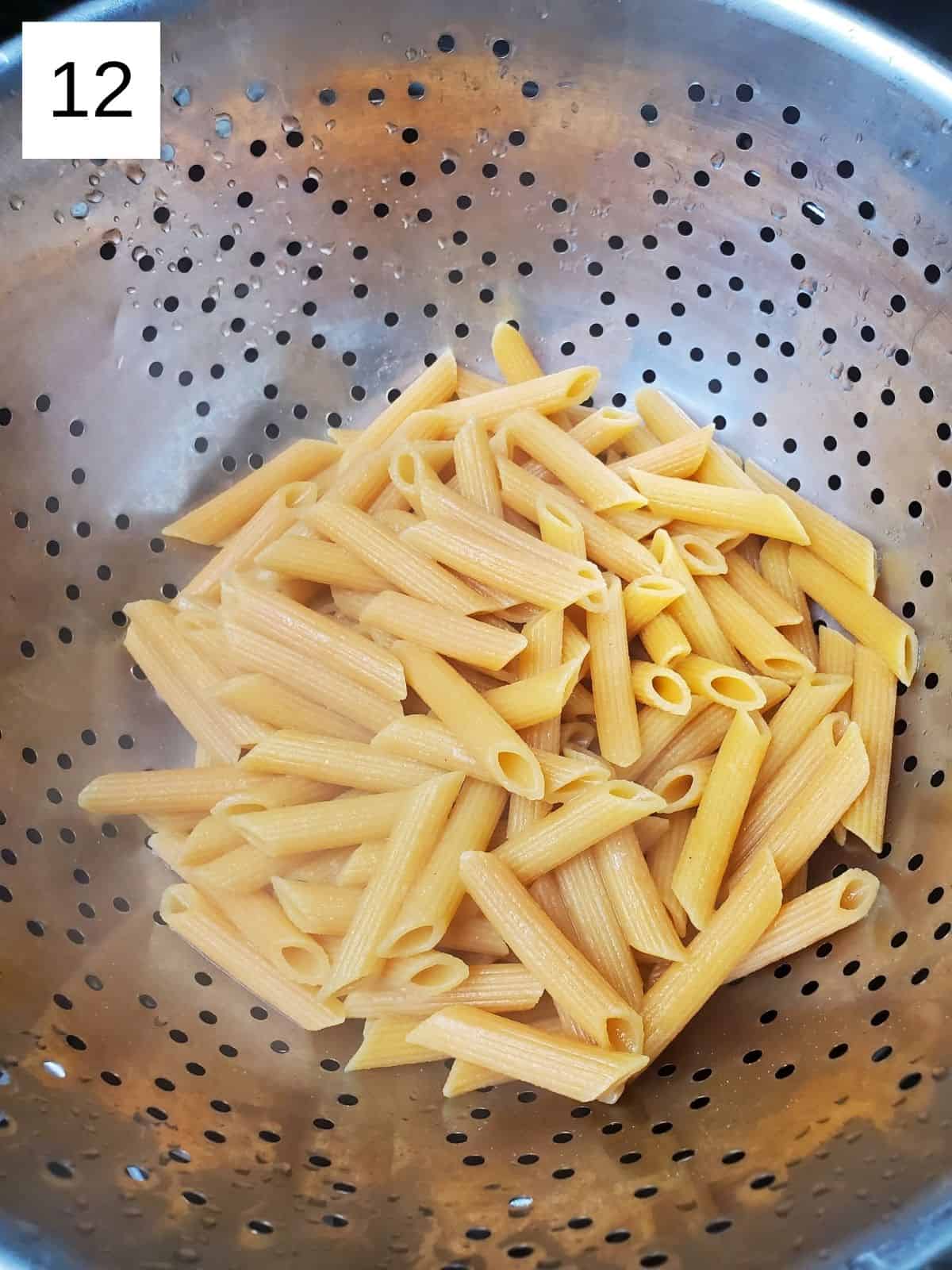 cooked red lentil penne pasta on a metal strainer.