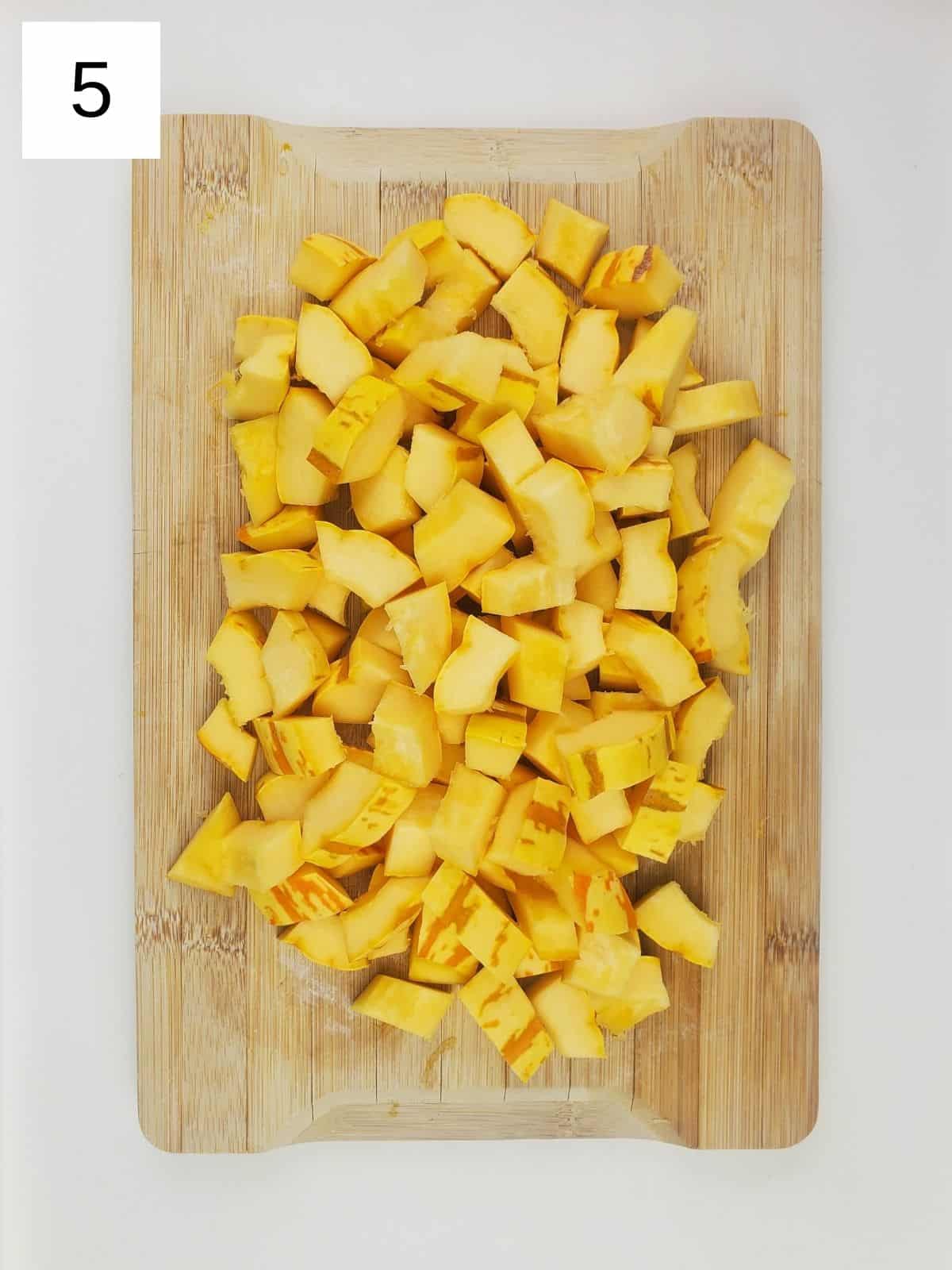 delicata squash cubes on a wooden cutting board.