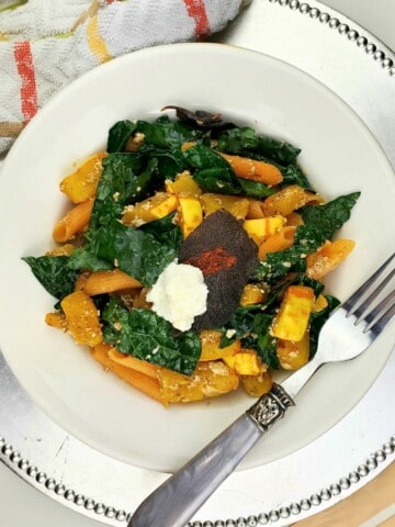 cooked delicata squash pasta with sage butter, ricotta cheese, and kale leaves served on a white plate.