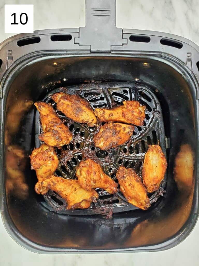 cooked spiced chicken wings in a single layer in the air fryer basket.