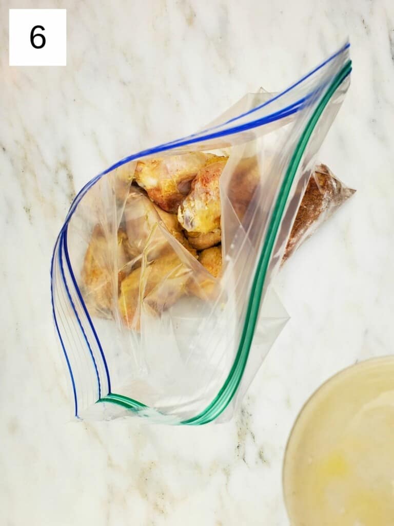 ziploc bag of chicken wings with spices and oil, on top of a marble slab.