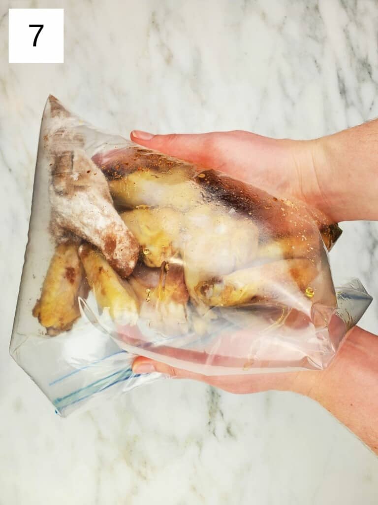 closed ziploc bag of chicken wings with spices and a large amount of air trapped, on top of a marble slab.