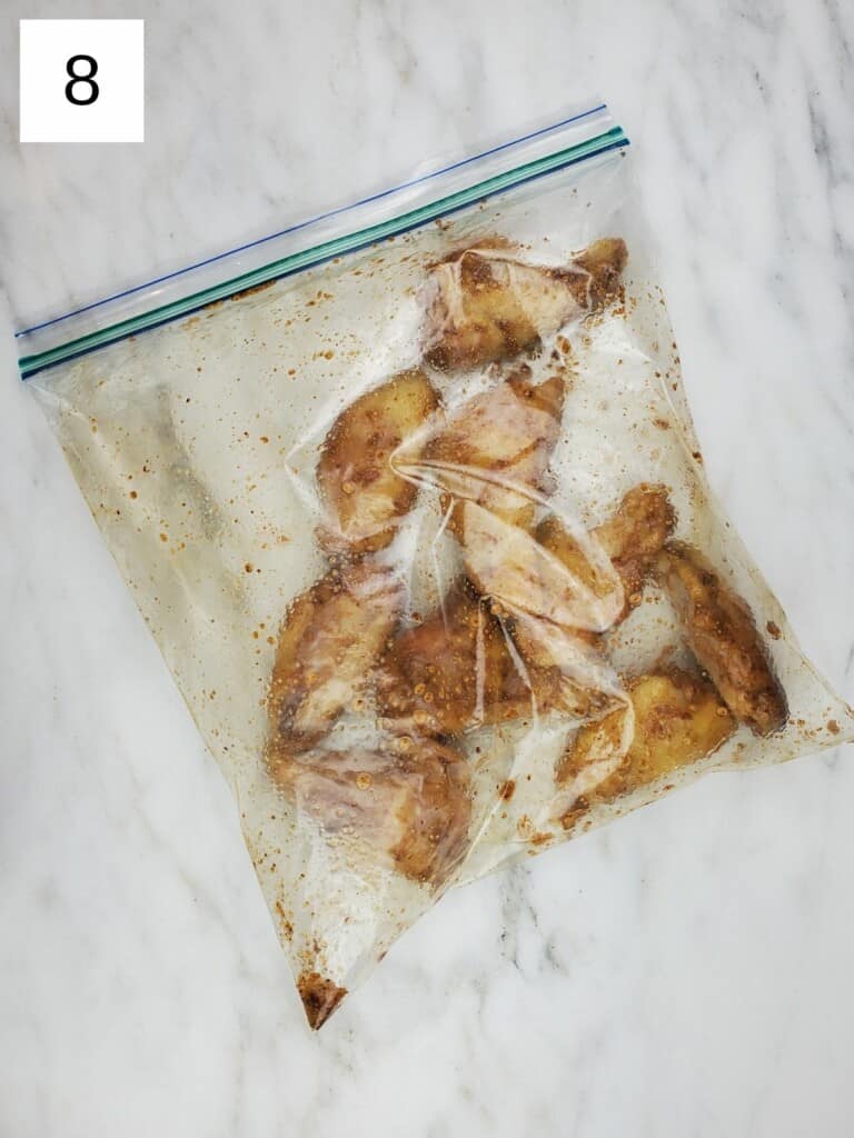 closed ziploc bag of chicken wings with spices, on top of a marble slab.