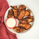 air-fried chicken wings arranged on one side of a white plate, served with white sauce, all on a white background.