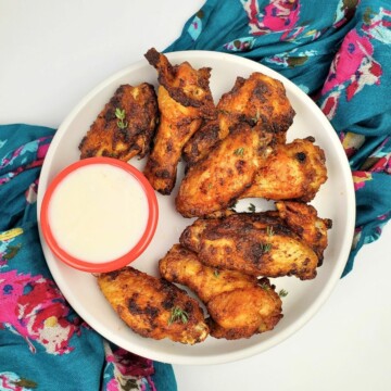 air-fried chicken wings arranged on one side of a white plate, served with white sauce, all on a white background.