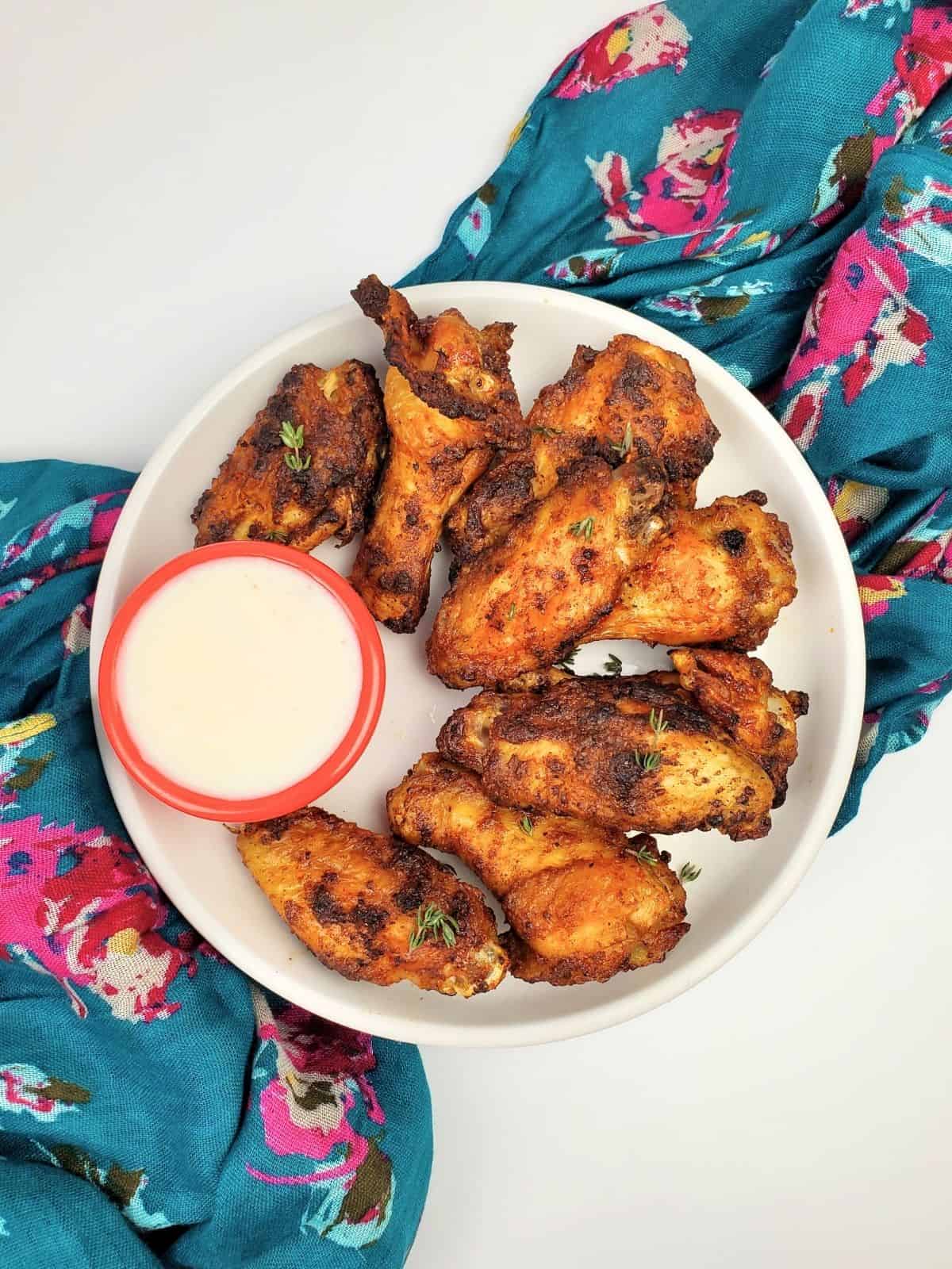 air-fried chicken wings arranged on one side of a white plate, served with white sauce, all on a white background.