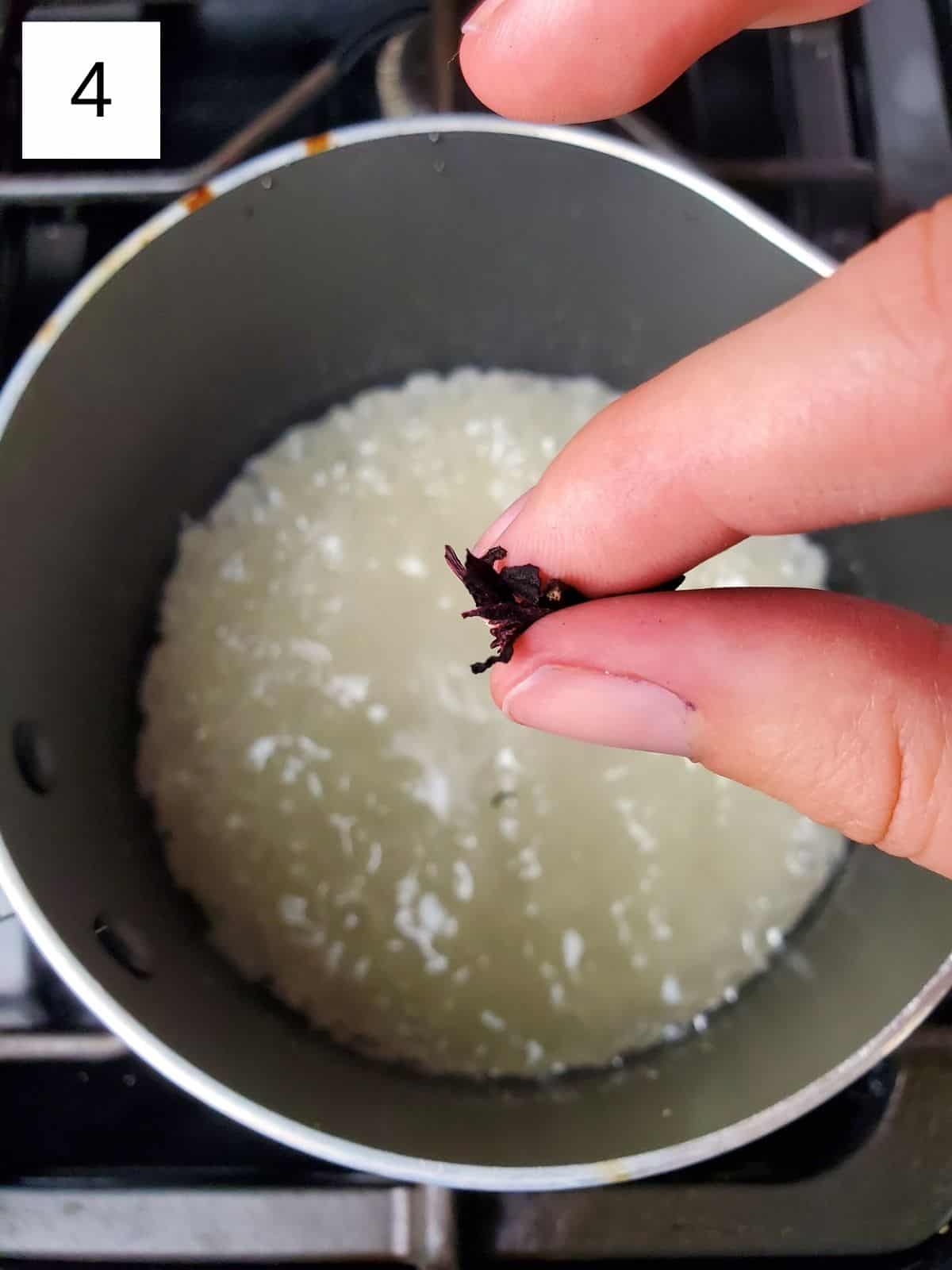 a pinch of hibiscus being poured into a pot of sugar mixture.