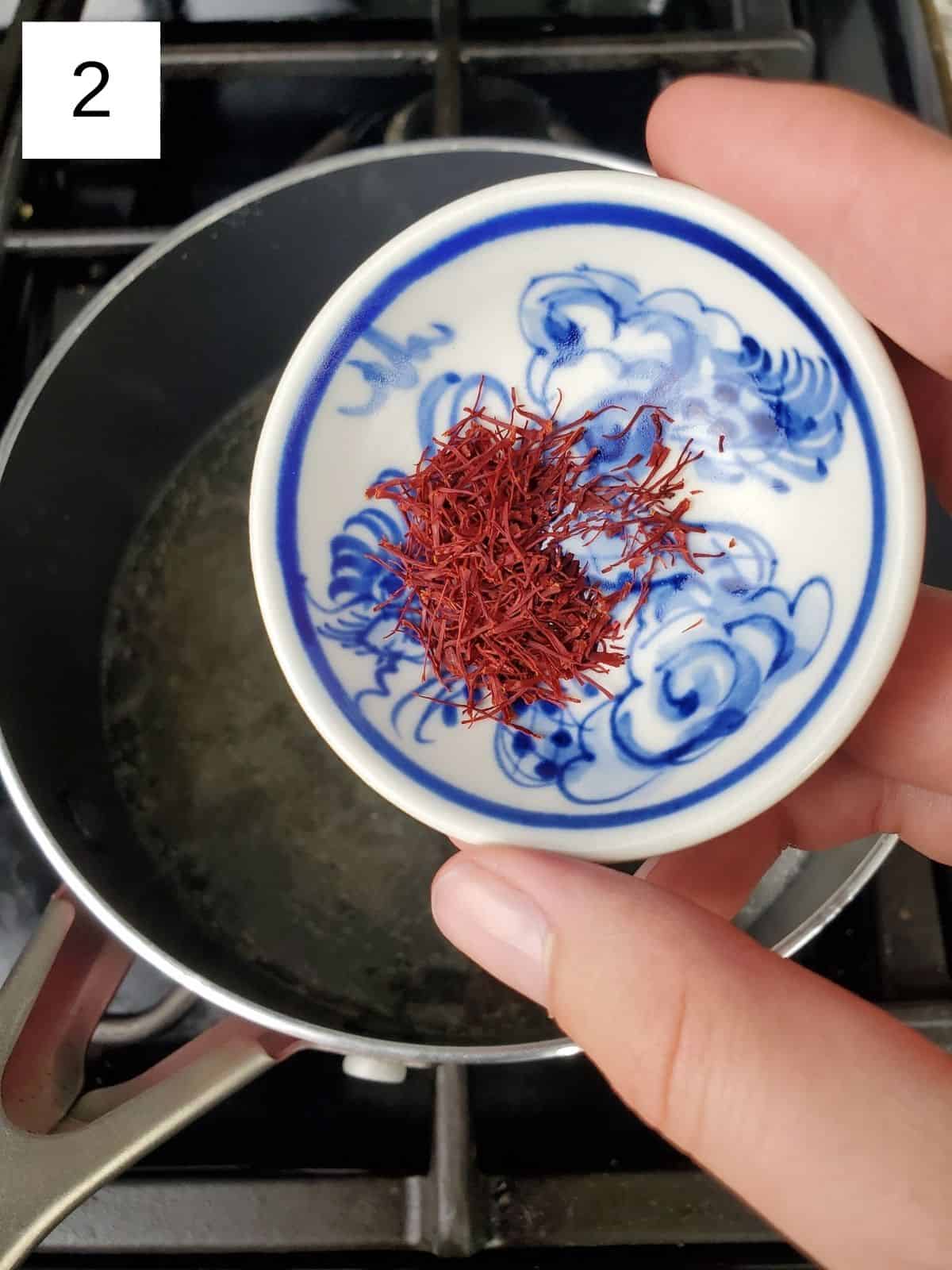 a pinch of saffron being poured into a pan of sugar and water mixture.