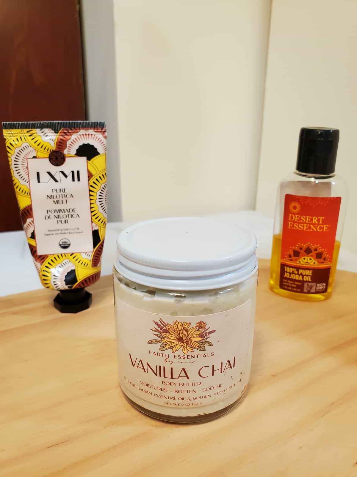 small container of chai-scented shea butter lotion with a small bottle of shea butter and a small container of jojoba oil in the background.