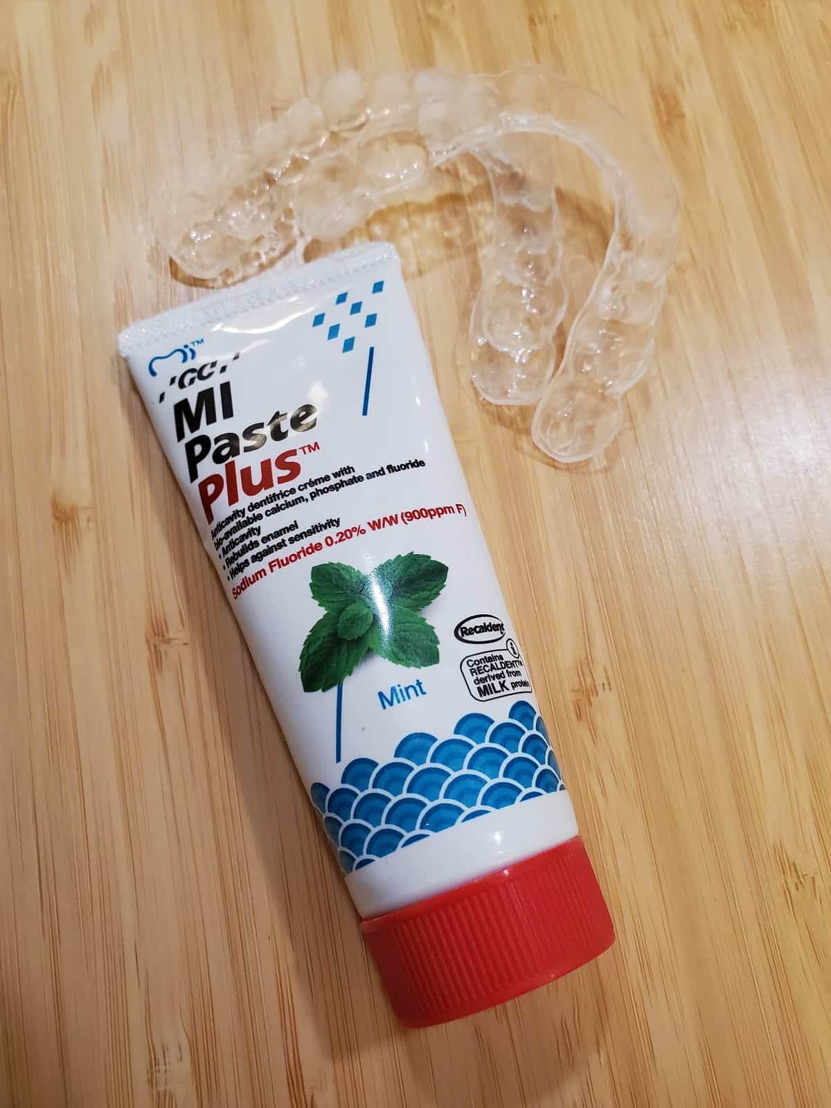 white bottle of MI Paste Plus on a wooden background.