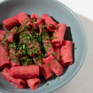 a bowl of cooked pasta, coated with beet sauce and topped with some herbs.