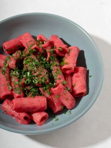 a bowl of cooked pasta, coated with beet sauce and topped with some herbs.