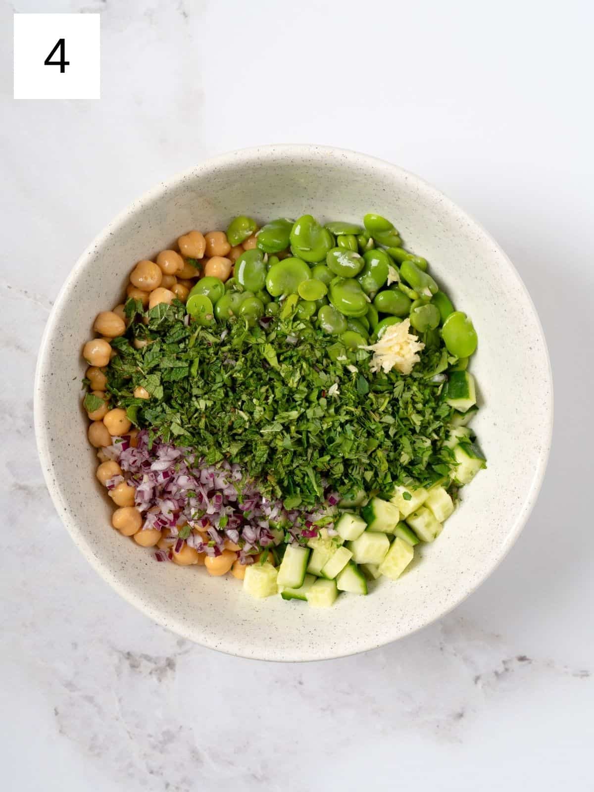 a mixture of chickpeas, fava beans, cucumber, herbs, and spices in a bowl.