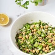 a bowl of fava bean and chickpea salad coated with salad dressing.