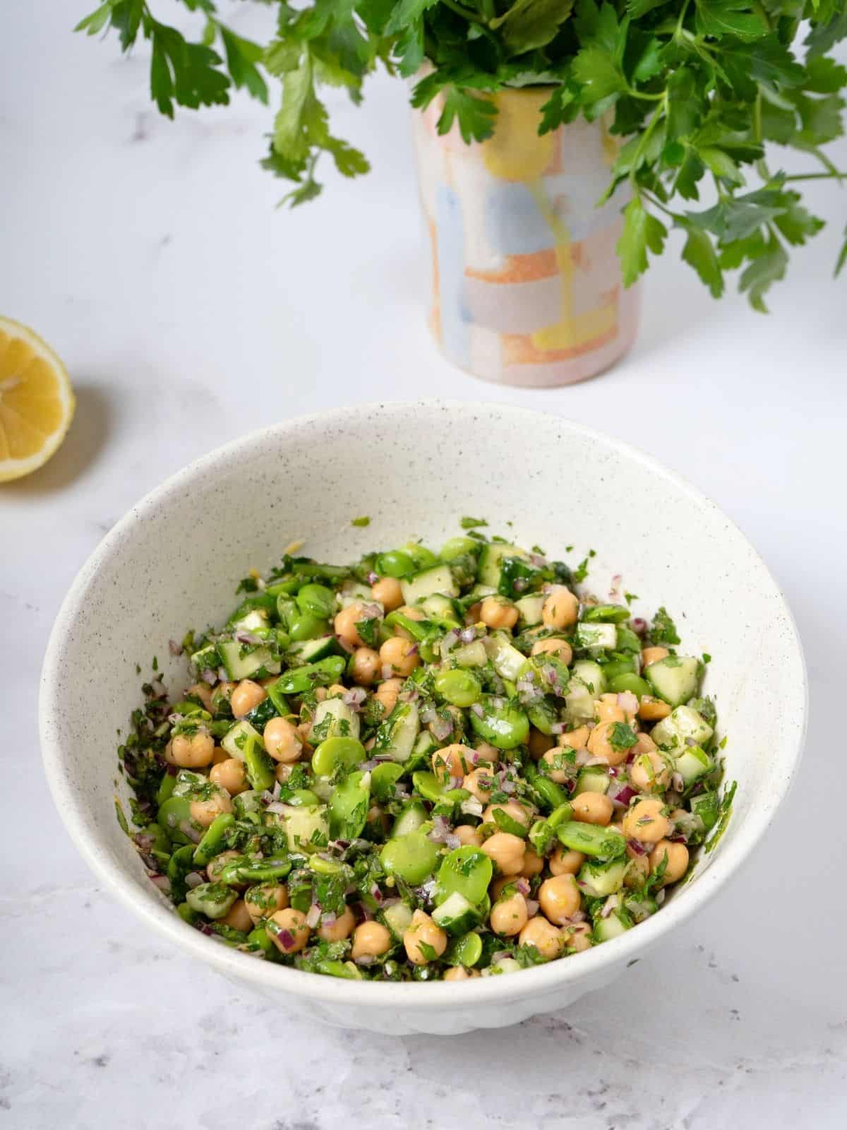 a bowl of fava bean and chickpea salad coated with salad dressing.