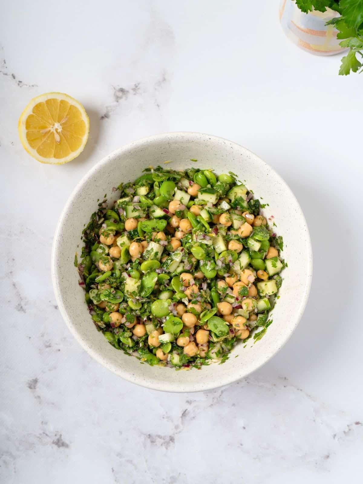 a bowl of fava bean and chickpea salad coated with salad dressing.
