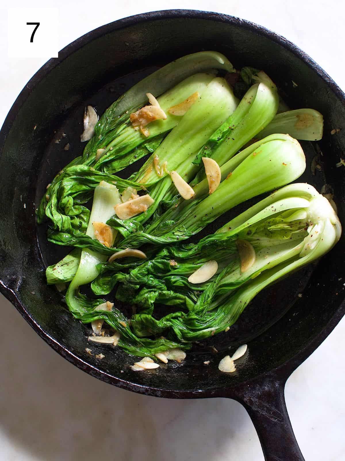 cooked bok choy seasoned with garlic, ginger, and other spices in a cast iron.