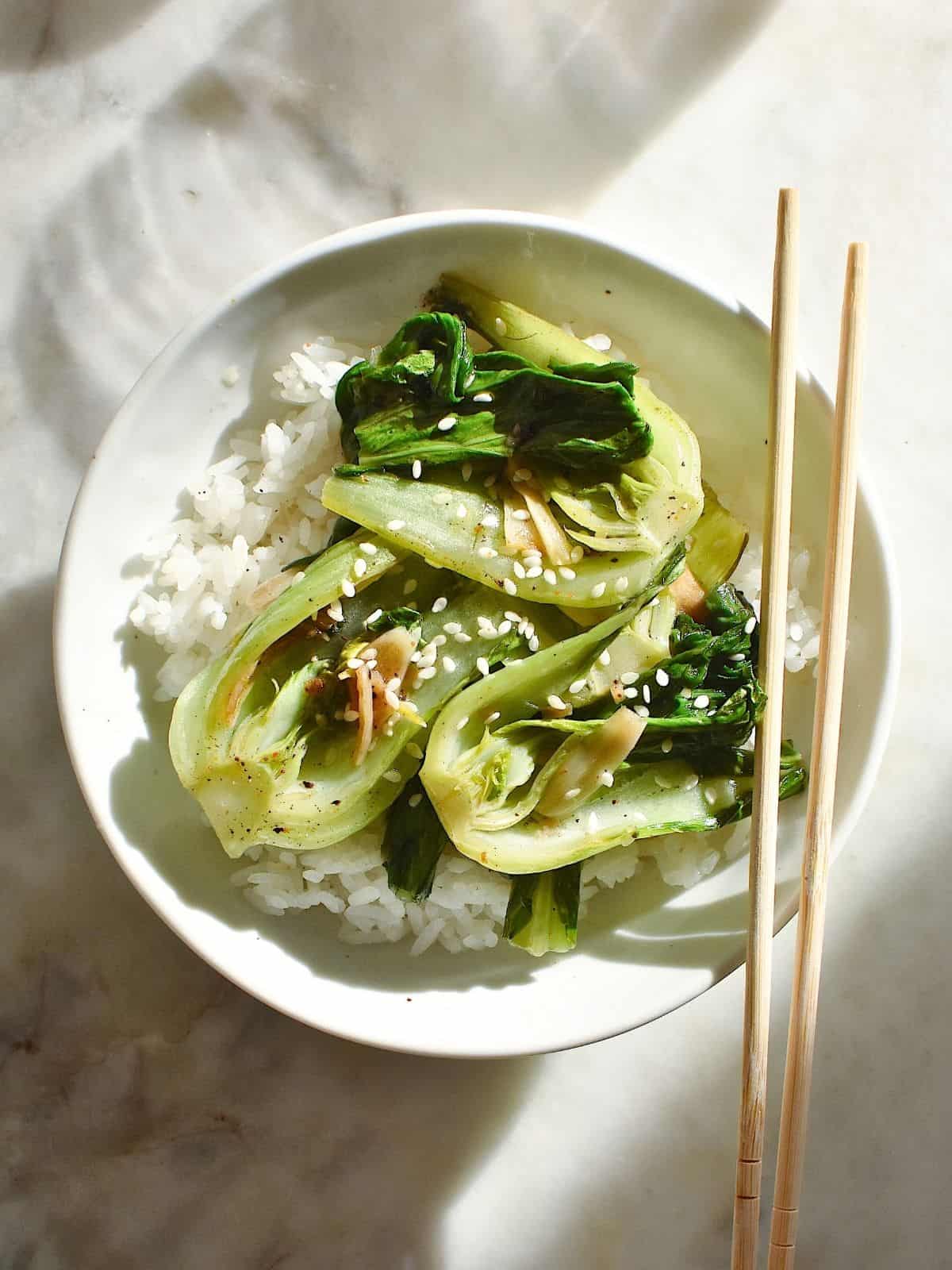 cooked, seasoned bok choy on a bowl of rice, topped with sesame seeds.