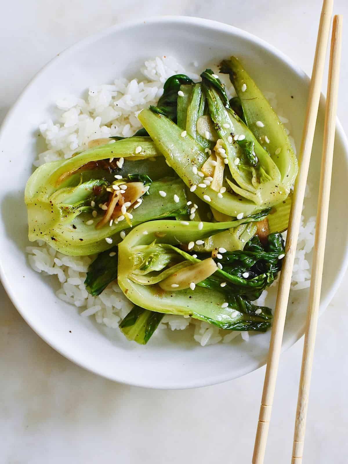 cooked, seasoned bok choy on a bowl of rice, topped with sesame seeds.