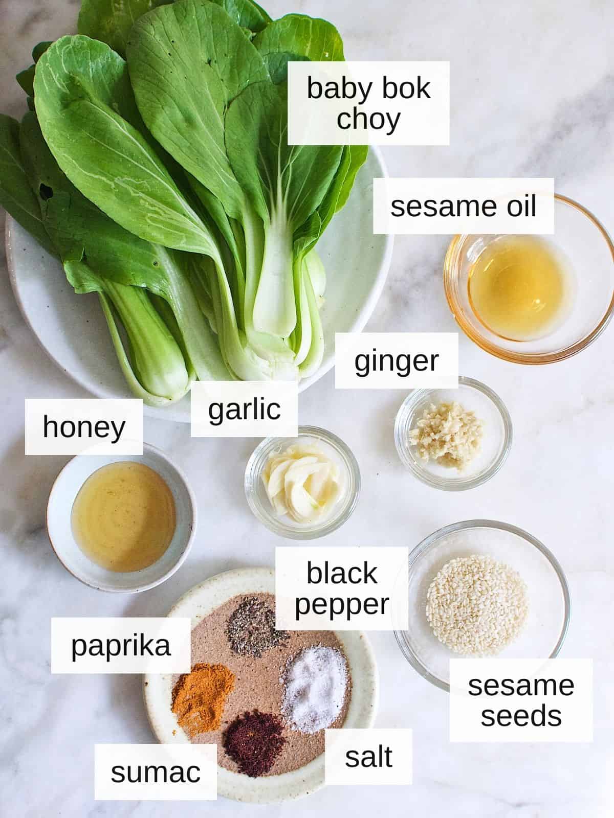 ingredients for garlic ginger bok choy recipe, including honey, pepper, sesame seeds, paprika, sumac, salt, garlic, sesame oil, ginger, and bok choy.