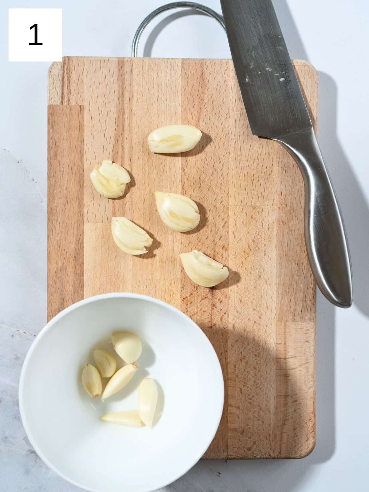 peeled garlic cloves on a wooden chopping board.