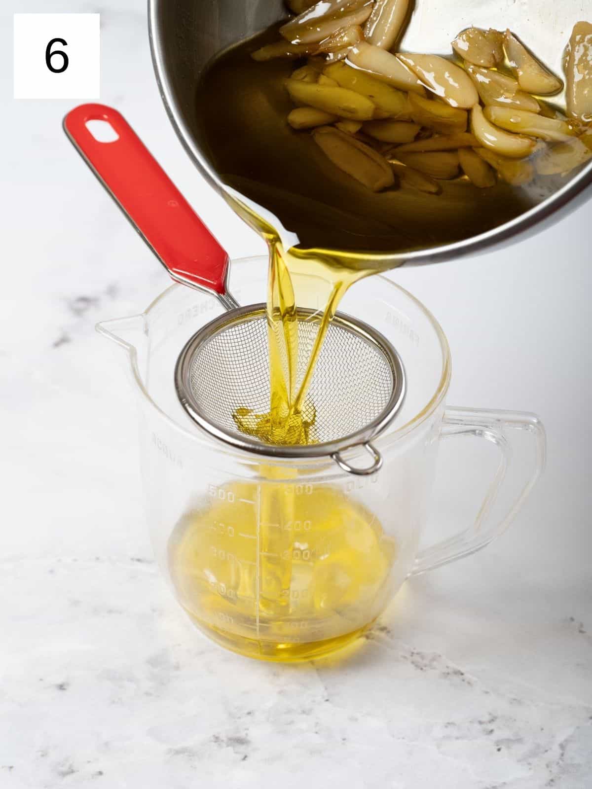 pouring garlic-infused olive oil through a sieve into a glass.