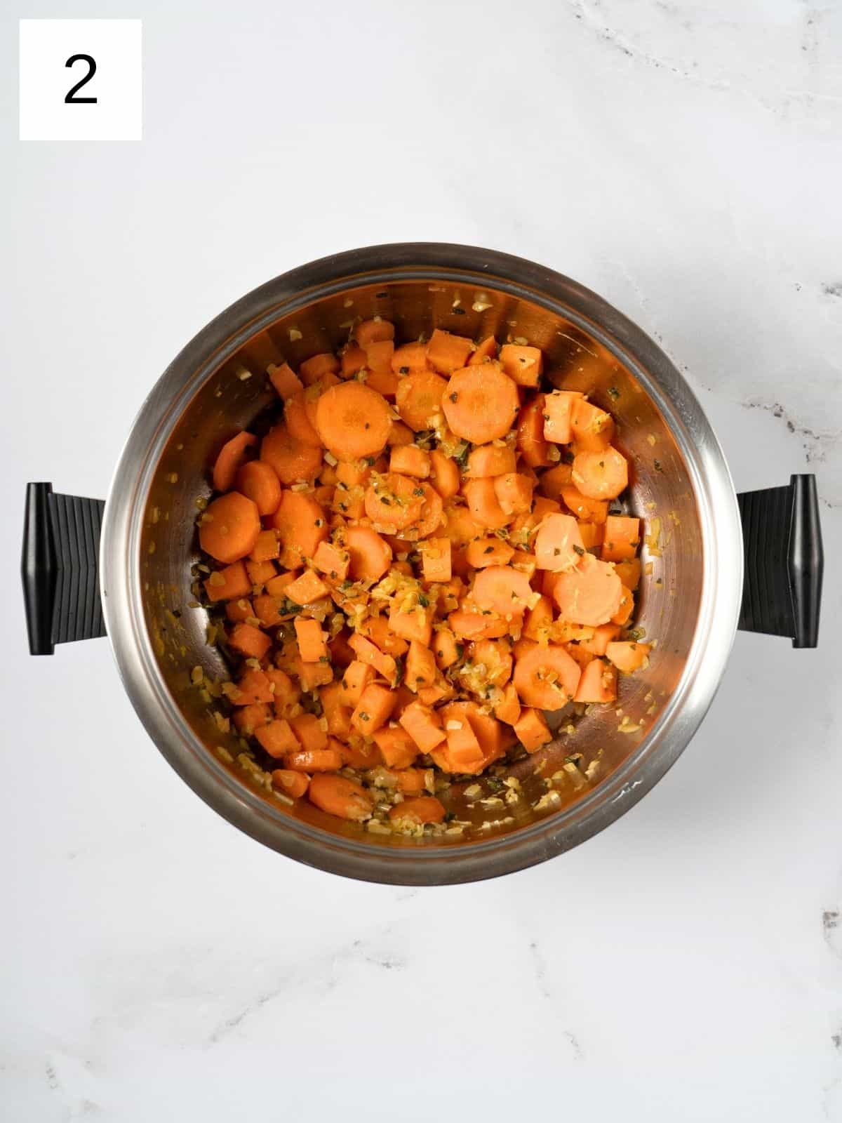 cubes sweet potatoes and sliced carrots, coated with sautéed herbs and spices, in a pot.