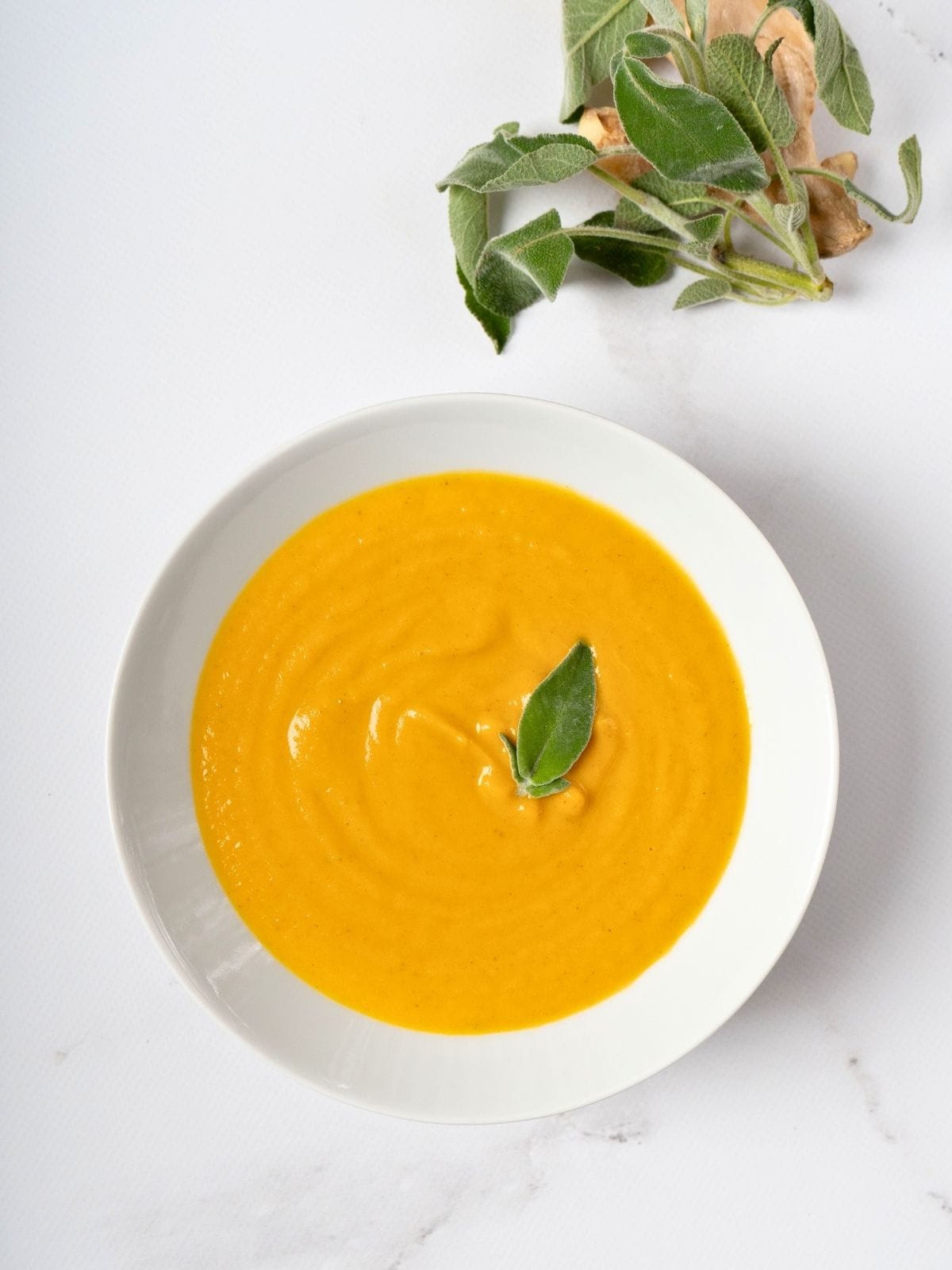 sweet potato and carrot soup, topped with fresh sage leaf, in a bowl.