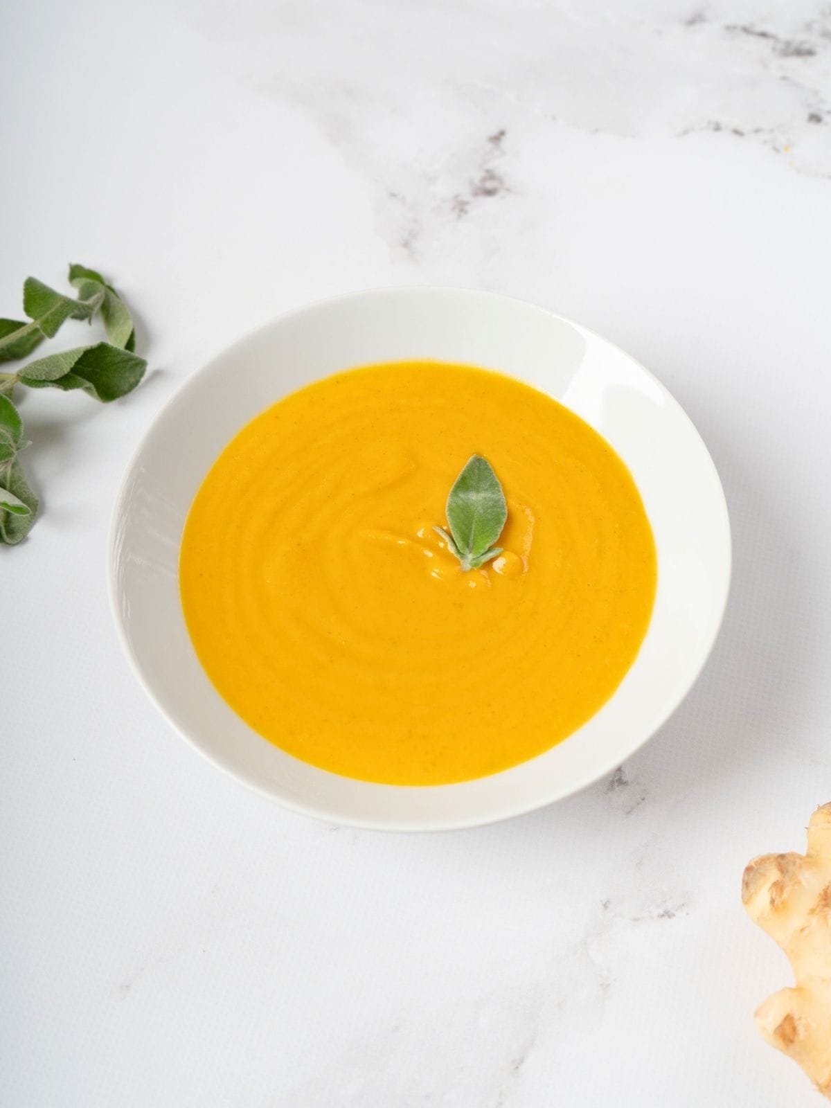 sweet potato and carrot soup, topped with fresh sage leaf, in a bowl.