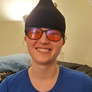 smiling person with a black ice pack worn on their head and orange-colored glasses on.