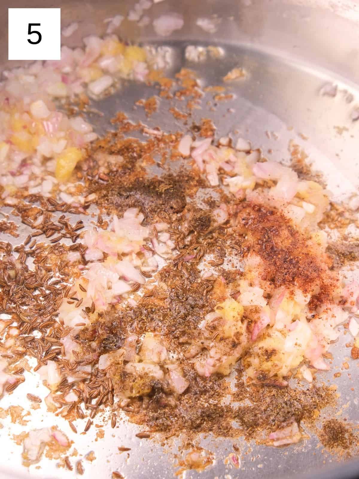 sautéed onions and ginger, along with cumin seeds, cardamom powder, and garam masala, in a pot.