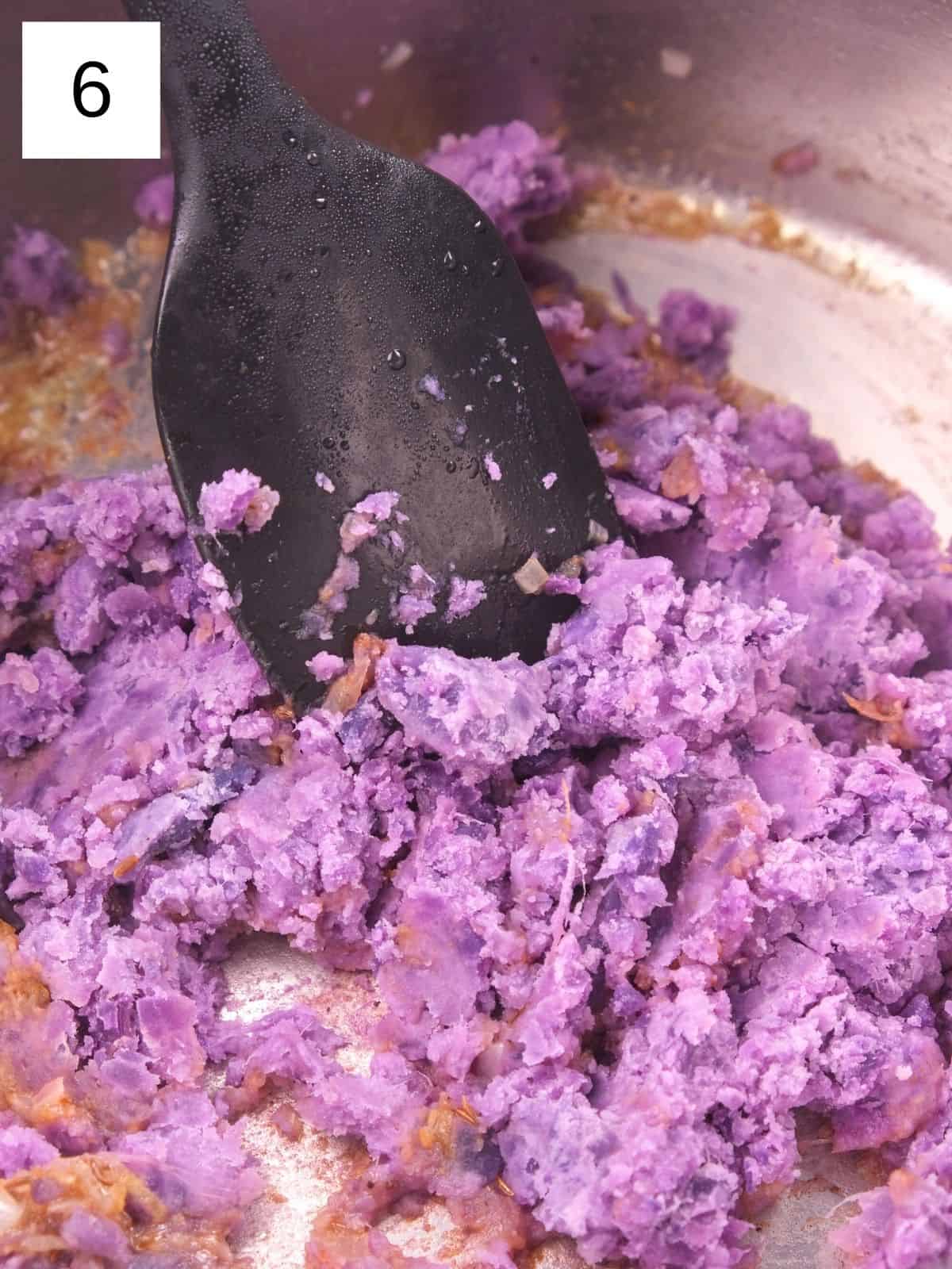 mashed purple sweet potato in a mixture of sautéed spices in a pot.