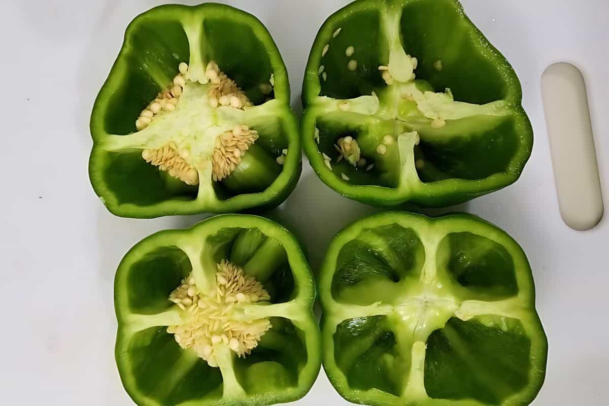 2 green bell peppers cut in half on a chopping board.