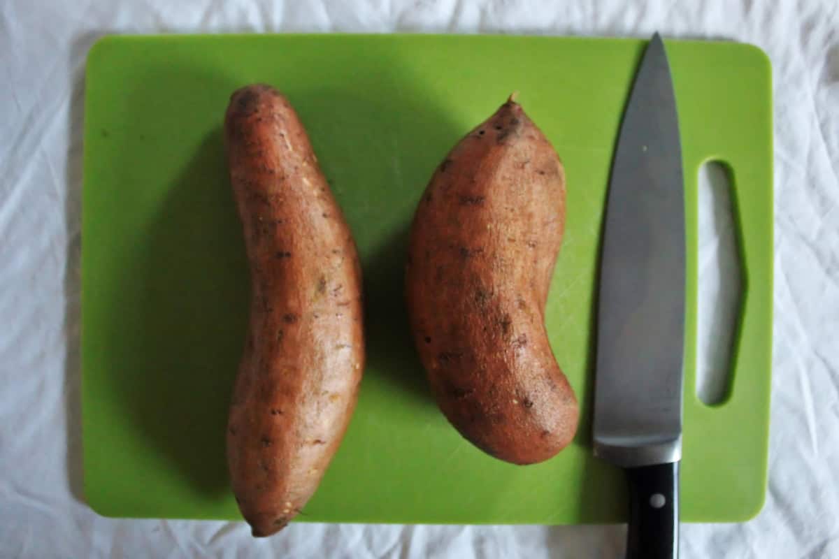 Sweet potatoes on a chopping board, next to a knife. 