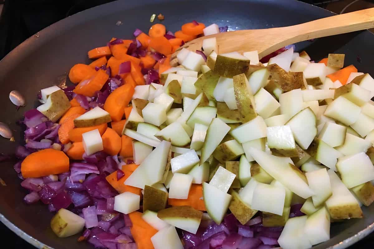 Diced carrots, onions, and potatoes being sautéed in a pan.