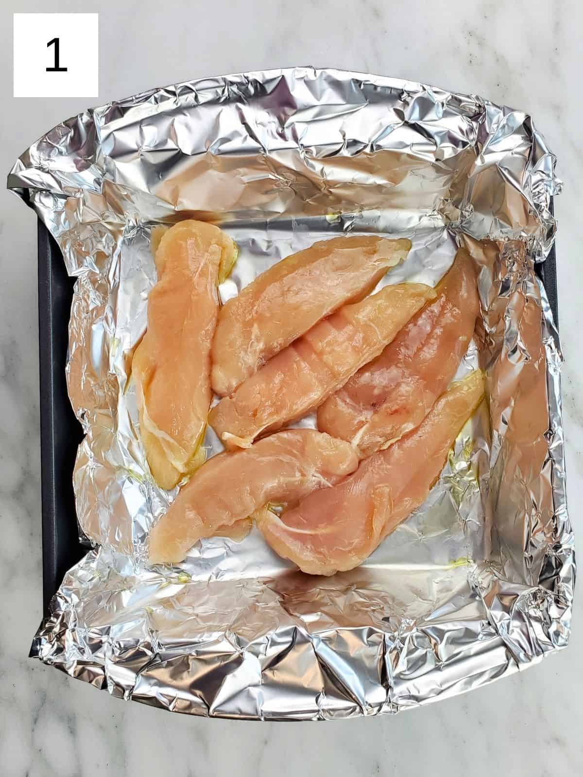 chicken tenders arranged on a foil-lined baking tray.
