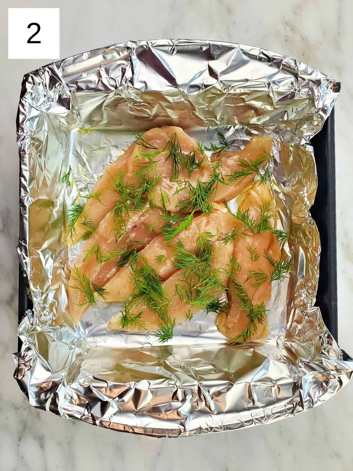 chicken tenders, topped with fresh dill, olive oil, and sea salt, arranged on a foil-lined baking tray.