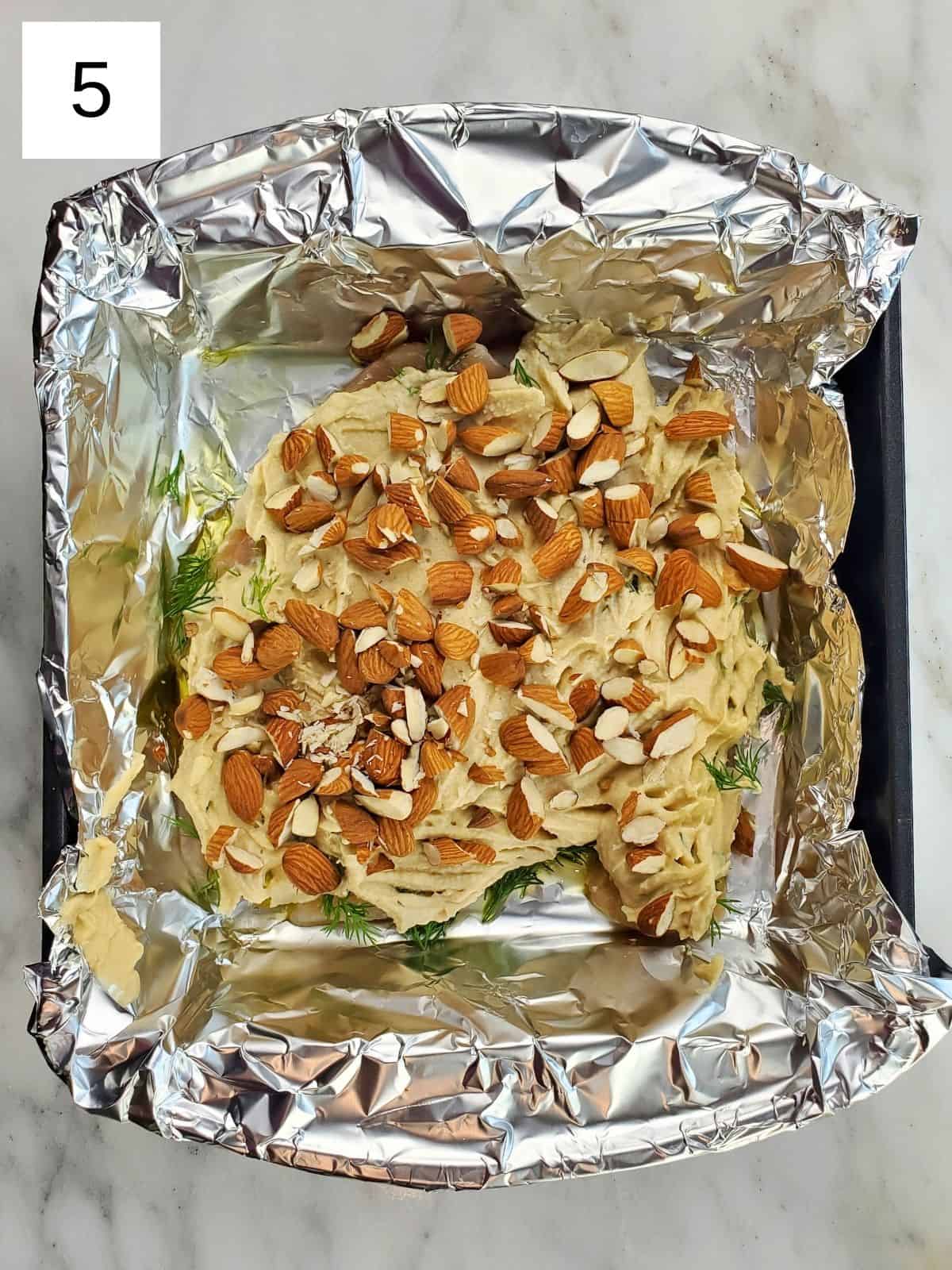 seasoned chicken tenders, topped with hummus and almonds, arranged on a foil-lined baking tray.