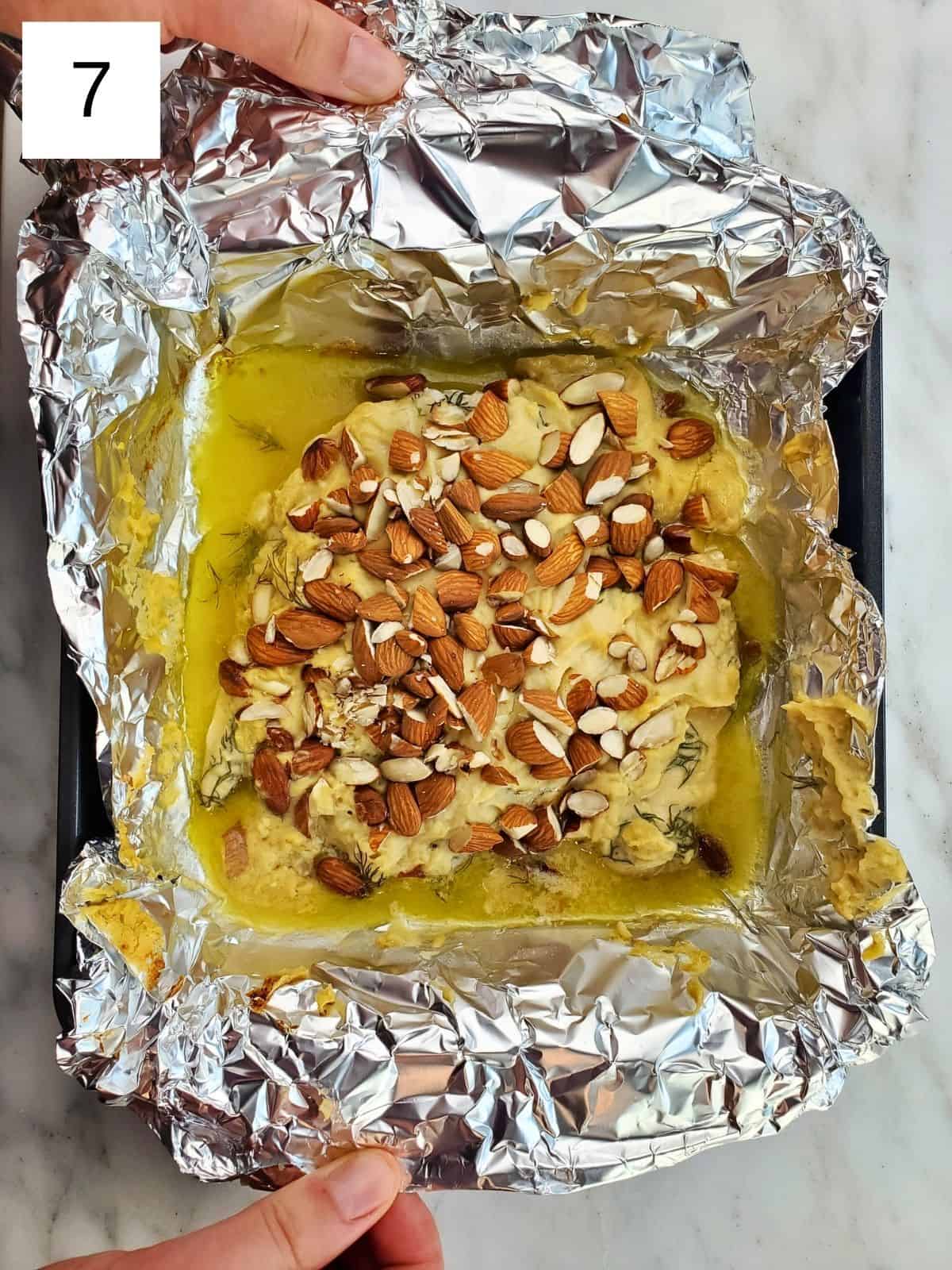 baked hummus-covered chicken on a foil-lined baking tray.
